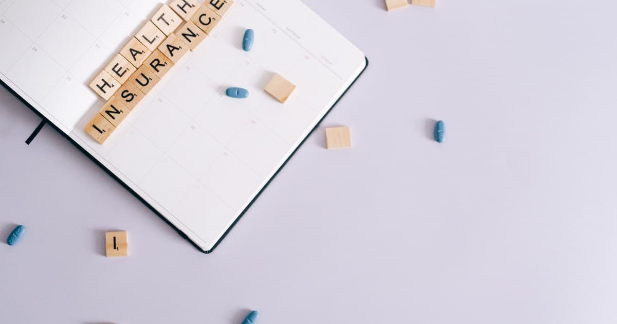 플래너 위에 HEALTH INSURANCE 스크래블 타일과 파란 알약들